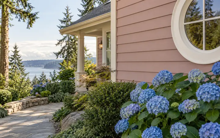 Dusty rose horizontal siding with cream trim and blue flowering plants.