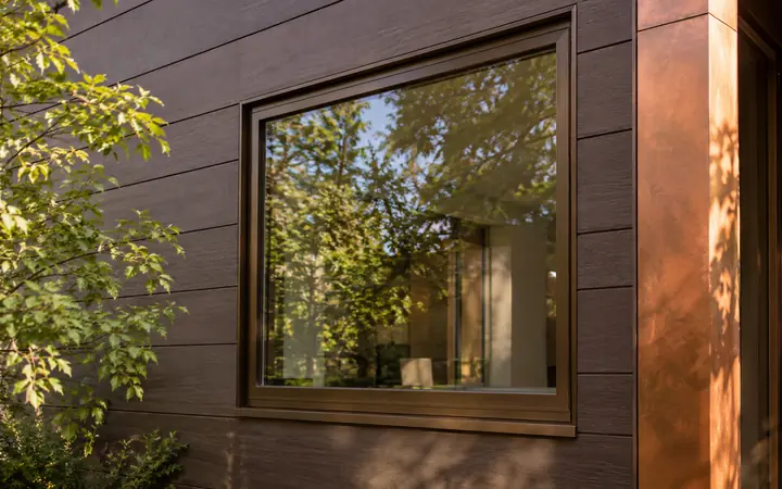 Bronze-framed rectangular window on cocoa-brown cladding beside copper-colored trim.