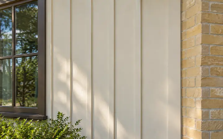 Cream vertical board-and-batten cladding beside bronze window trim and a butter-yellow brick return.