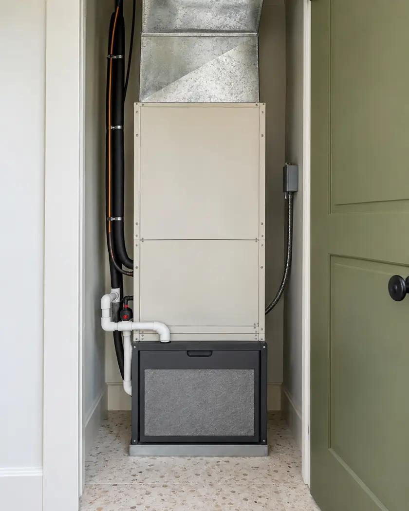 Cream indoor HVAC unit with gray ductwork and a dark base cabinet in an olive-trimmed utility closet.