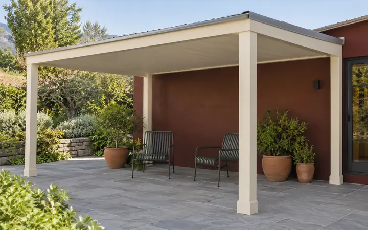 Cream freestanding patio cover with a pale-gray metal roof above green chairs and terracotta pots.