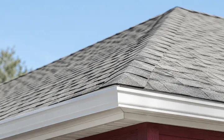 Pale-gray asphalt shingles meeting wide white fascia above a burgundy wall.