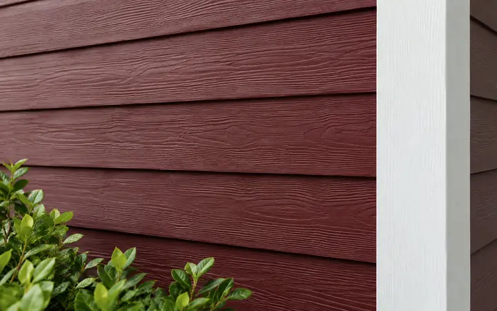 Deep burgundy horizontal lap wall with white vertical corner trim and green planting.