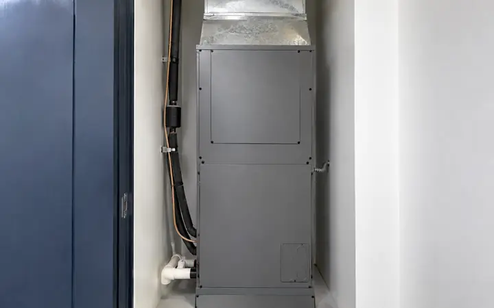Graphite-gray indoor air-handler cabinet with a metal duct above in a white utility alcove.
