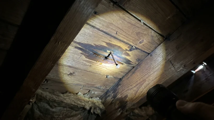 Dark water stains on the underside of wooden attic decking.