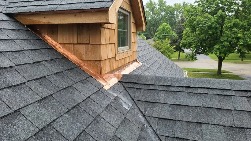 Close-up of clean shingle cuts and flashing in a roof valley near a dormer window.